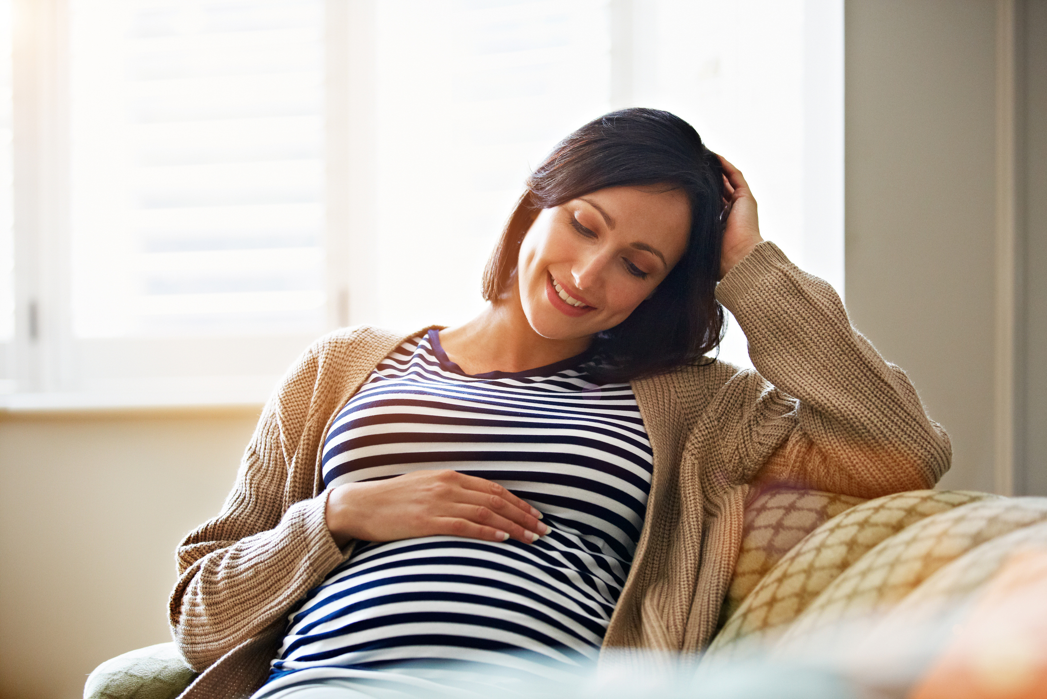 a smiling pregnant woman sitting on her sofa holding her stomach