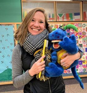A picture of Robyn Maestas smiling with a toothbrush and dinosaur puppet