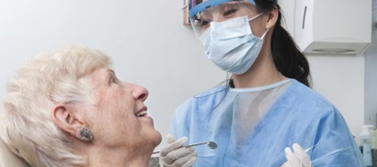 A female dental hygienist smiles and talks with an elderly female patient as she prepares to work on her teeth. Description from Getty images