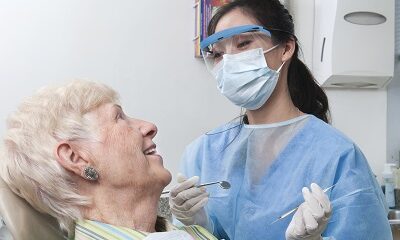 A female dental hygienist smiles and talks with an elderly female patient as she prepares to work on her teeth. Description from Getty images