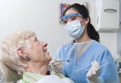 A female dental hygienist smiles and talks with an elderly female patient as she prepares to work on her teeth. Description from Getty images
