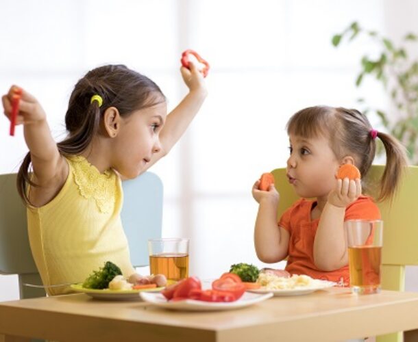 Two little girls eating healthy foods and juice with their meal