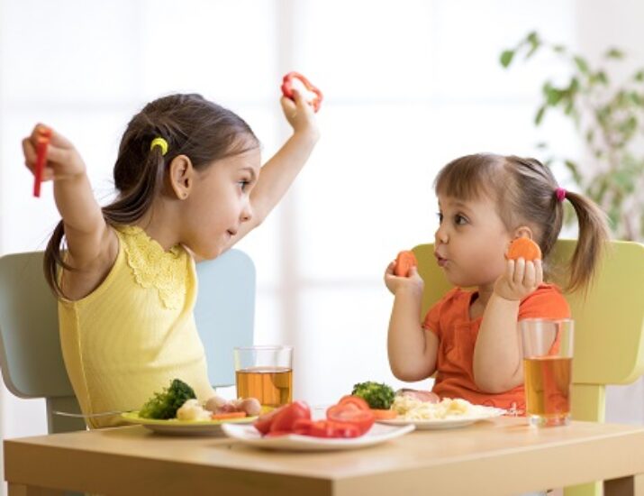 Two little girls eating healthy foods and juice with their meal