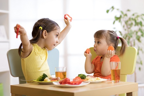 Two little girls eating healthy foods and juice with their meal