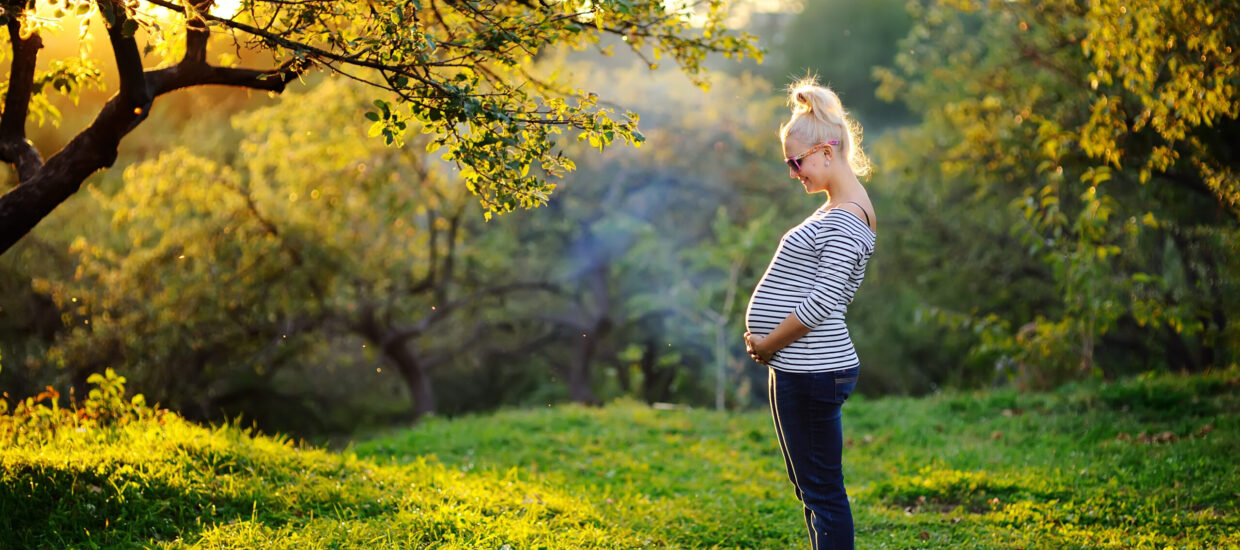 Pregnant person cradling stomach standing outside