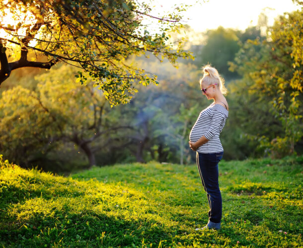 Pregnant person cradling stomach standing outside