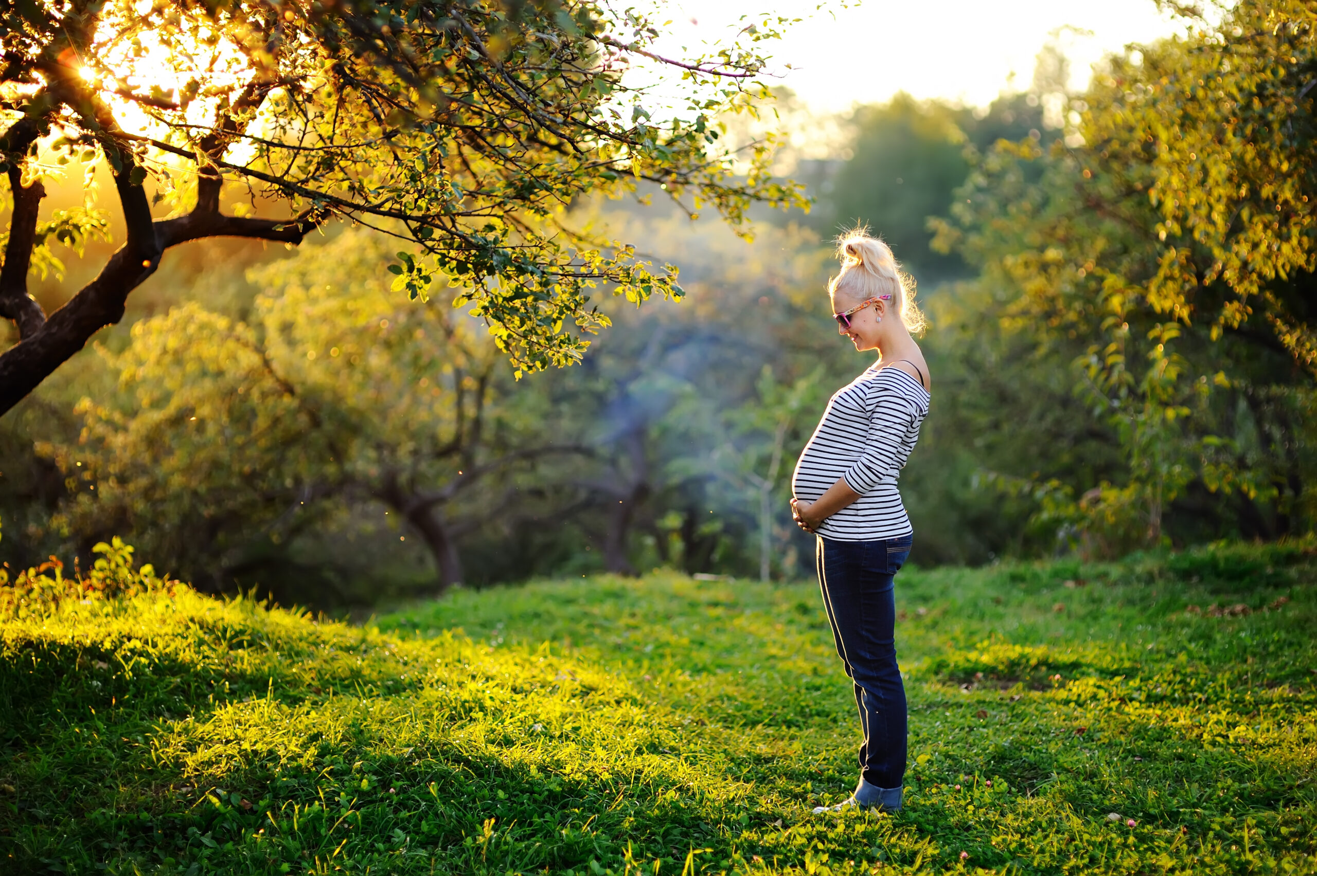 Pregnant person cradling stomach standing outside
