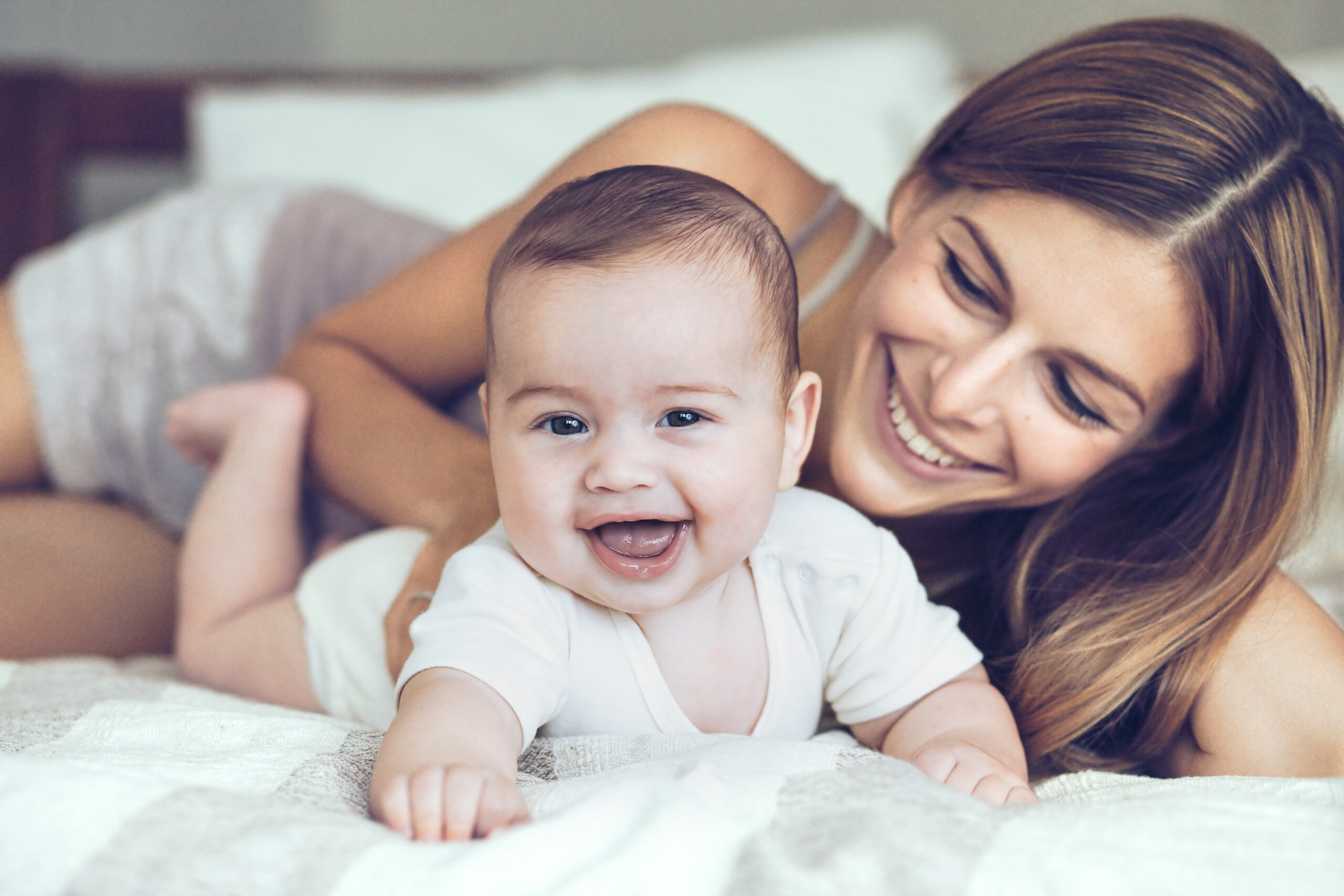 Mother and baby laying on bed and smiling