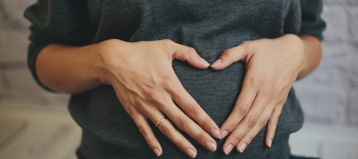 Pregnant person making a heart on stomach with hands